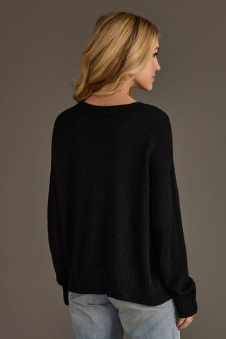 A woman shown from the back wearing a black knit sweater and light blue jeans against a solid dark gray studio background.