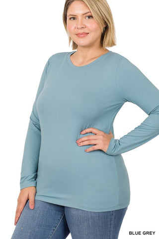 A woman modeling a long-sleeve crewneck top in a dusty blue-gray color, paired with blue jeans, against a plain white background.