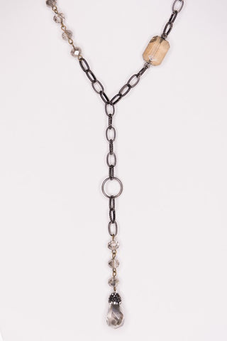 A long Y-shaped chain necklace featuring dark gunmetal links, clear faceted beads, a rectangular beige stone, and a dangling teardrop-shaped clear stone, shown against a plain white background.