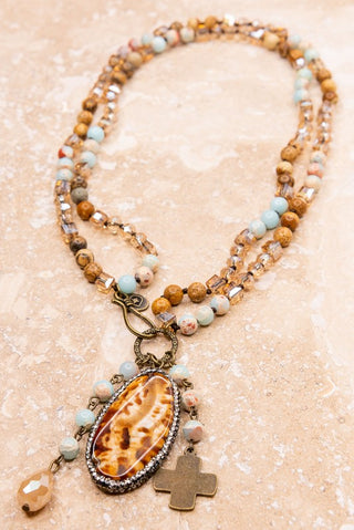 Necklace with shell pendant and cross charm on a beige background