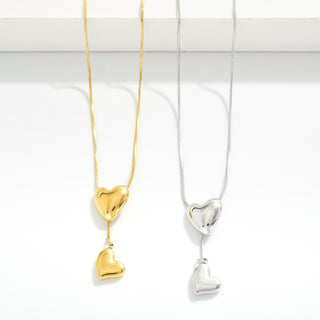 Two heart-shaped pendants on necklaces, one gold and one silver, against a white background.
