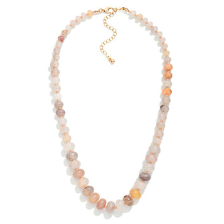 A beaded necklace made of round, polished stone beads in soft peach, pink, cream, and light gray tones, with a gold-tone clasp and extender chain, shown on a plain white background.