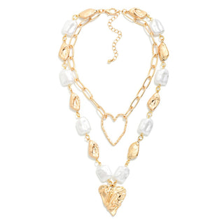 A gold-toned double-strand necklace featuring textured gold and polished white stone beads, a central gold heart outline pendant, and a larger textured gold heart drop at the bottom, displayed on a clean white background.