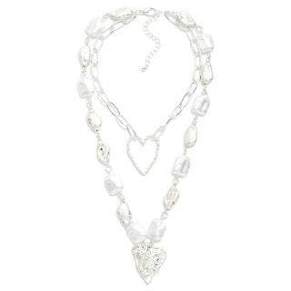 A silver-toned multi-strand necklace featuring irregular white baroque pearls, a heart-shaped wire pendant, a larger heart charm, and a dangling heart pendant, displayed on a clean white background.