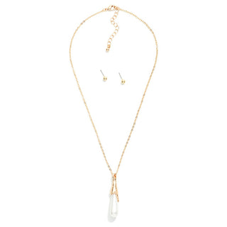 A delicate gold chain necklace with a long drop pendant made of two crossed gold bars holding a white teardrop-shaped stone, shown with matching stud earrings on a plain white background.