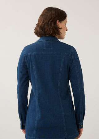 A woman with shoulder-length brown hair is shown from the back wearing a dark blue denim shirt jacket against a plain light gray studio background.