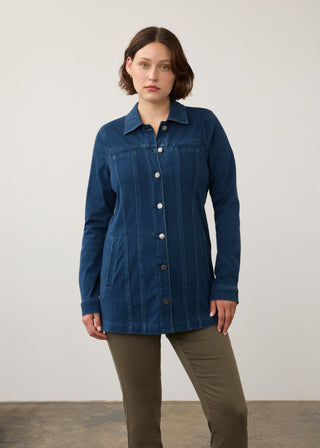 A woman modeling a dark blue denim button-up shirt jacket with vertical channel stitching, paired with olive green pants, against a plain light gray studio background.