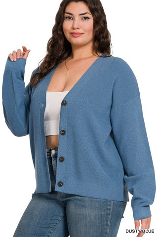 A woman wearing a dusty blue button-front cardigan over a white ribbed crop top and blue jeans, photographed against a plain white studio background. The text 'DUSTY BLUE' appears in the bottom right corner.