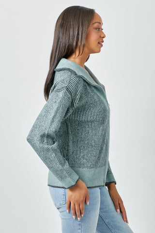 Woman wearing a green knitted sweater and light blue jeans on a white background