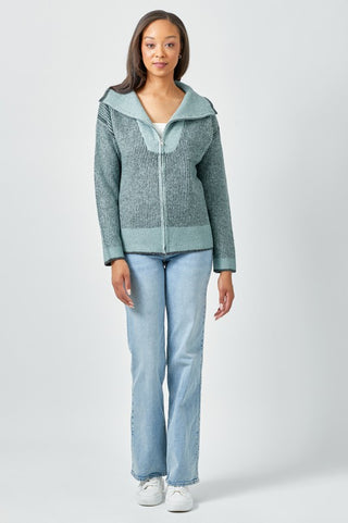 Woman wearing a green zip-up sweater and light blue jeans on a white background