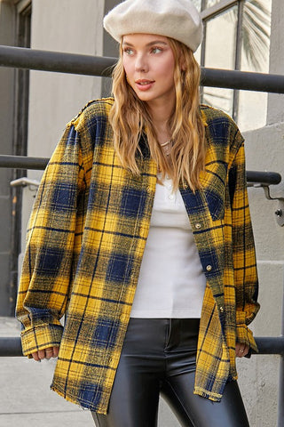 Woman wearing a yellow and blue plaid shirt, white top, and black pants outdoors.