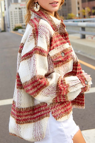 A woman wearing a chunky, oversized plaid jacket in cream, rust red, and brown tones, paired with white shorts, photographed outdoors on a city street.