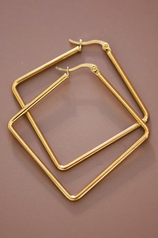A pair of gold-toned square hoop earrings with fishhook backings, displayed on a solid brown background.