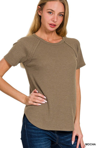 A woman modeling a short-sleeve waffle-knit top in a muted taupe-brown color, paired with blue jeans, against a plain white background.