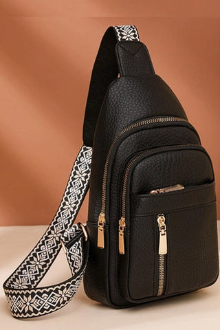 Black sling bag with patterned strap on a beige background