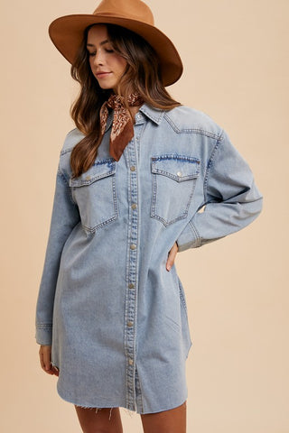 A woman wearing a light-wash blue denim shirt dress with a brown wide-brim hat and a brown patterned neck scarf, posed against a solid beige background.