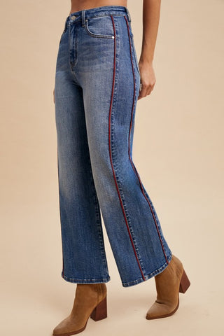 Blue jeans with red stitching worn by a person on a beige background