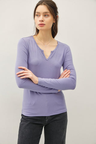 Woman wearing a purple long-sleeve top with a V-neckline against a plain background