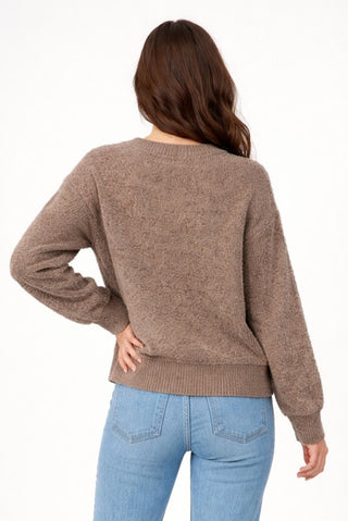 A woman shown from the back wearing a brown knit sweater and light blue jeans against a plain white background.
