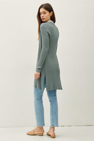 Woman wearing a long green cardigan and light blue jeans on a white background