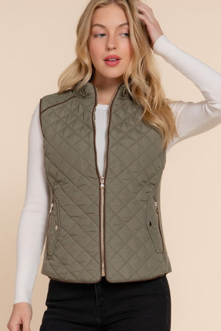 Woman wearing an olive green quilted vest on a beige background