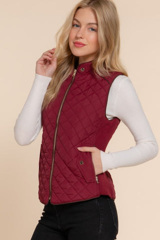 Woman wearing a wine colored quilted vest on a beige background
