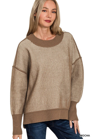 A woman wearing a long-sleeve knit sweater with vertical ribbed texture in a warm taupe-brown color, paired with blue jeans, against a plain white background.