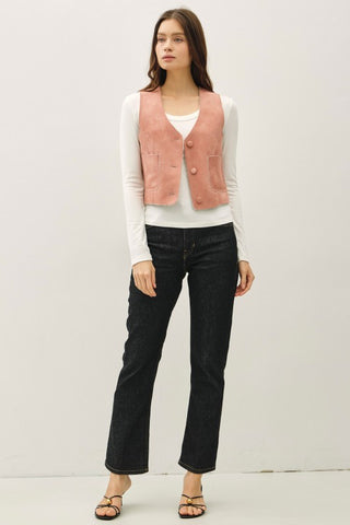 Woman wearing a pink vest over a white shirt with black pants on a plain background