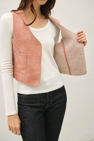 Person wearing a white shirt, black pants, and a pink vest on a plain background