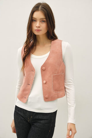 Woman wearing a pink vest over a white shirt on a plain background