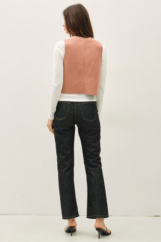 Woman wearing a pink vest, white shirt, black jeans, and black shoes on a plain background