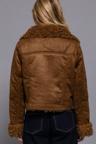 Brown suede jacket with fur trim worn by a person on a gray background