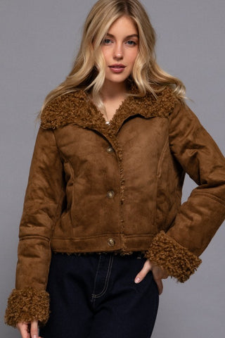 Woman wearing a brown suede jacket with fur trim against a gray background