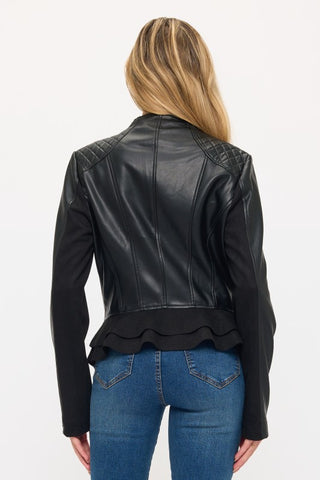 A woman viewed from the back wearing a black faux-leather cropped jacket with quilted shoulder details and a ruffled hem, paired with blue jeans against a plain white background.