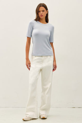 Woman wearing a light blue top and white pants on a plain background
