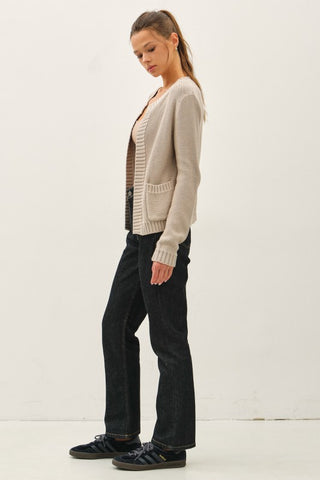 Woman wearing a beige cardigan, black pants, and black shoes on a white background