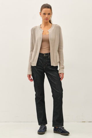 Woman wearing a beige cardigan, beige top, black pants, and black shoes on a white background