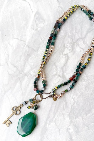 Necklace with green pendant and key charm on a textured white background