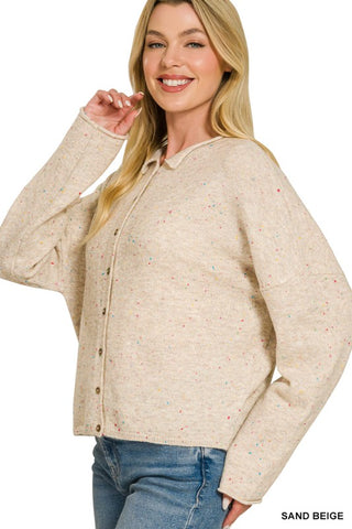 A woman wearing a light sand beige long-sleeve button-up cardigan with tiny multicolor speckles, paired with blue jeans, against a plain white background.