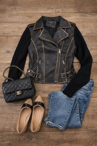 Black leather jacket, black shirt, quilted handbag, beige flats, and blue jeans on a wooden surface