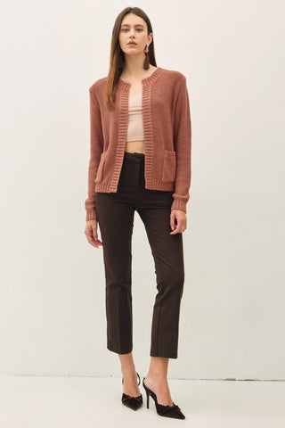 Woman wearing a brown cardigan, beige top, black pants, and black high heels on a white background