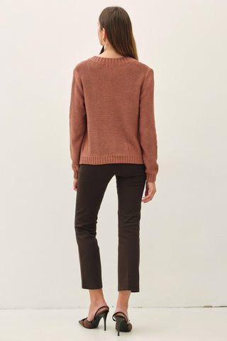 A woman shown from the back wearing a dusty rose knit sweater, dark brown cropped pants, and black high heels against a plain white studio background.