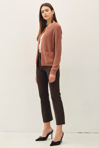 A woman modeling a dusty rose cardigan sweater, black cropped trousers, and black pointed-toe heels against a plain white studio background.
