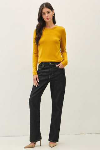 A woman modeling a mustard yellow long-sleeve knit top and black wide-leg jeans against a plain white background.