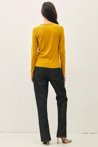 Person wearing a yellow long-sleeve top and dark jeans on a white background