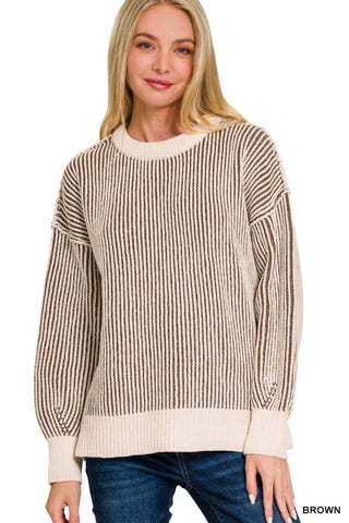 A woman wearing a brown and cream vertically striped knit sweater with a crew neck and ribbed cuffs and hem, paired with blue jeans, against a plain white background.