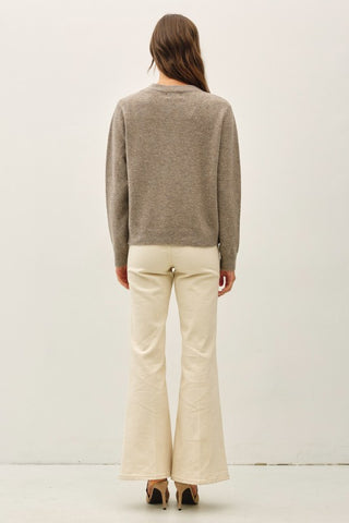 Back of a woman wearing a brown sweater, white pants and heels
