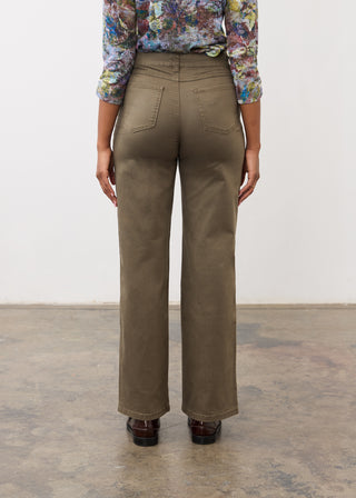 A person shown from the back wearing olive green wide-leg trousers, a colorful floral long-sleeve top, and dark brown shoes, standing against a plain white wall and concrete floor.