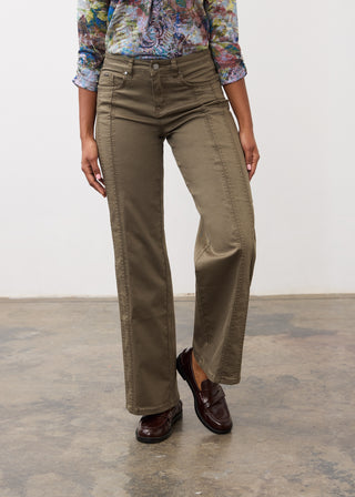 A person wearing olive green wide-leg pants, a colorful floral long-sleeve shirt, and dark brown leather loafers, standing against a plain white wall and concrete floor.