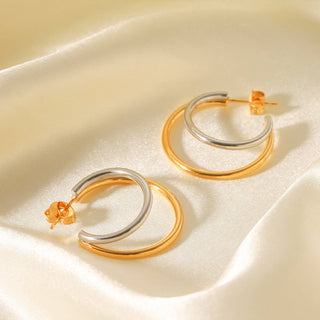 Pair of gold and silver hoop earrings on a beige fabric background